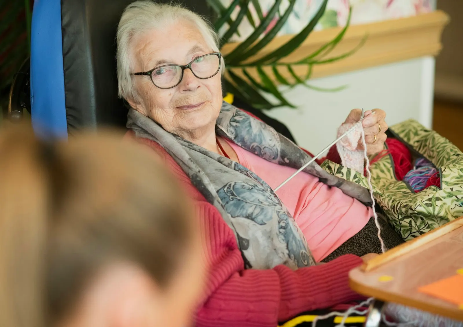 Ältere Dame strickt zufrieden in ihrem Sessel – ein selbstbestimmtes Leben zuhause.